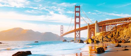 Blick vom Baker Beach auf die Golden Gate Bridge in San Francisco, mit Meer, Felsen im Vordergrund und Küstenlandschaft bei sonnigem Himmel.