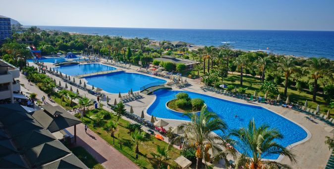 Blick auf mehrere Schwimmbecken in einer Hotelanlage mit Palmen und Meer im Hintergrund