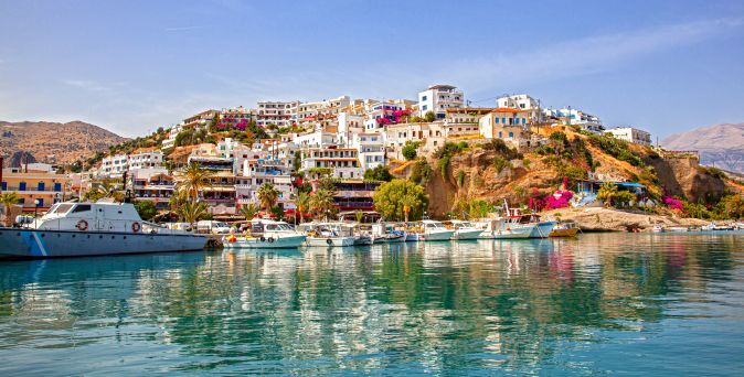 Hafen mit Booten vor einem Hügel mit dicht bebauten weißen Häusern und blühenden Bougainvillea in Sitia auf Kreta
