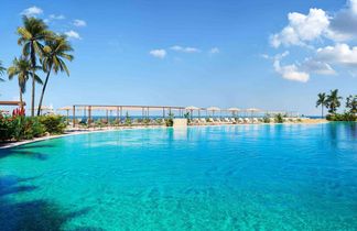 Großer Außenpool mit klarem Wasser, umgeben von Liegestühlen und Sonnenschirmen, blauer Himmel mit wenigen Wolken.