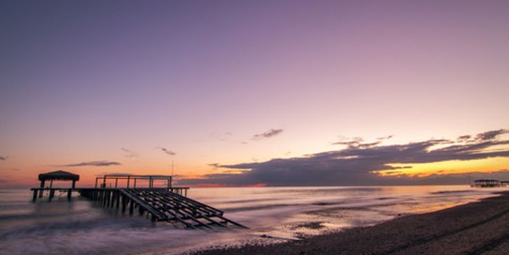 Verlassener Holzsteg am Strand von Belek in der Türkei bei Sonnenuntergang, ruhiges Meer und violett-orangefarbener Himmel