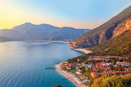 Panoramablick auf die Küste von Ölüdeniz in der Türkei mit türkisblauem Meer, Sandstrand, grünen Bergen und einer malerischen Ferienanlage im Vordergrund
