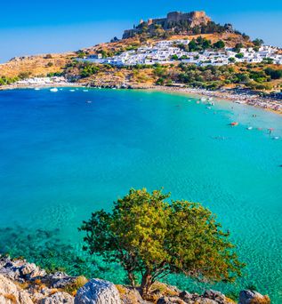Bucht mit türkisfarbenem Wasser, Segelboot, felsigem Ufer und weißem Dorf unter einer Burg auf einem Hügel.