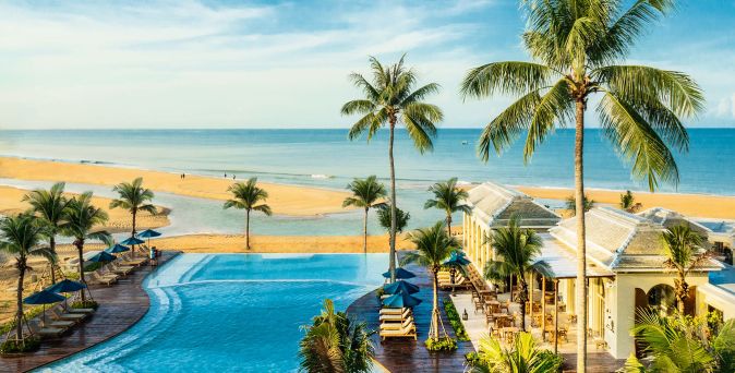 Blick auf den Poolbereich mit Palmen und Liegen des Devasom Khaolak Beach Resort & Villas am Strand unter blauem Himmel