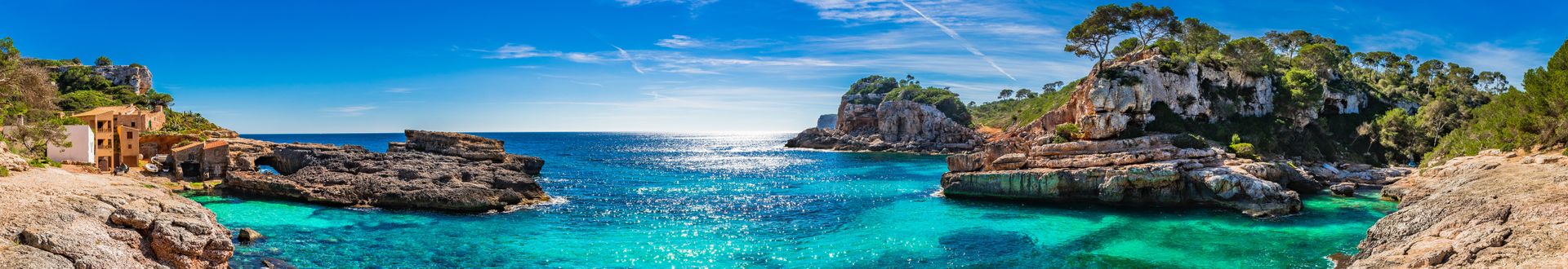 Malerische Bucht Cala s’Almunia auf Mallorca mit türkisblauem Wasser, Felsen und Pinienhainen unter klarem Himmel