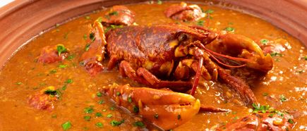 Ein gekochter Hummer liegt in einer Schale mit kräftiger Suppe und Kräutern