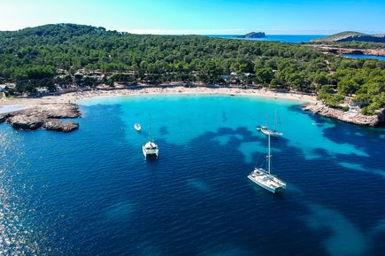 Beliebte Badebucht Cala Bassa mit weißen Sandstränden, türkisblauem Wasser und Segelbooten