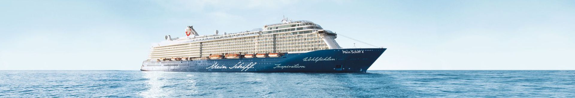 Das Kreuzfahrtschiff Mein Schiff 4 fährt auf dem Meer und ist seitlich unter klarem Himmel abgebildet.