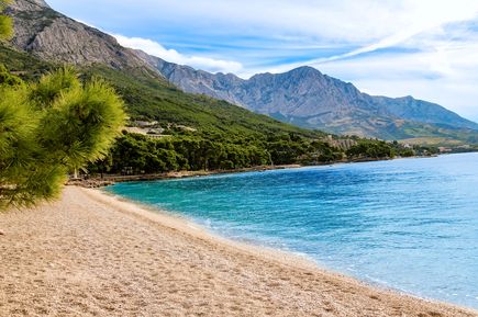Kiesstrand Punta Rata in Brela, Kroatien, mit kristallklarem Wasser, mediterranen Pinien und dem beeindruckenden Biokovo-Gebirge im Hintergrund