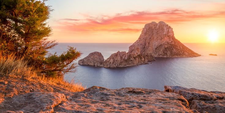 Blick auf den Felsen Es Vedrà vor Ibiza im Sonnenuntergang mit rötlich gefärbtem Himmel