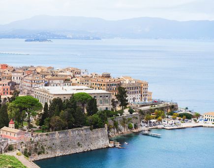 Blick auf die Altstadt von Korfu mit historischen Gebäuden, einer Stadtmauer und dem Hafen am Meer im Vordergrund