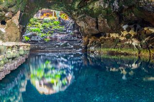 Wasserbecken in einer natürlichen Höhle mit steinernen Stufen und Pflanzen am Eingang