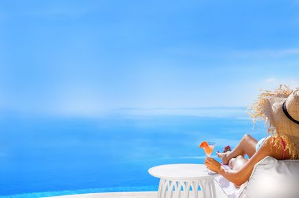Person mit Strohhut entspannt am Pool mit Cocktail in der Hand und Blick auf den blauen Himmel