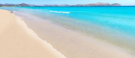 Feiner Sandstrand von Can Picafort auf Mallorca mit flachem türkisfarbenem Wasser und sanften Wellen