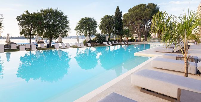 Großer Außenpool des Hyatt Ziva Corfu auf Korfu mit Sonnenliegen, Sonnenschirmen und mediterraner Gartenanlage direkt am Wasser
