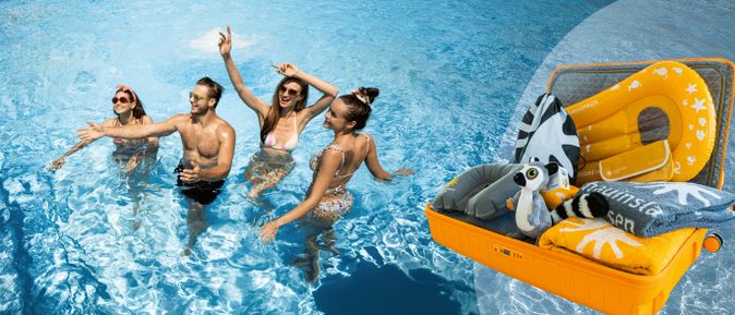 Vier junge Menschen in Badebekleidung, die im Wasser eines Schwimmbeckens stehen und lachen, davor ein geöffneter oranger Koffer mit verschiedenen Reiseutensilien wie Handtüchern, aufblasbarem Surfboard, Tickettasche, Plüschtier etc.