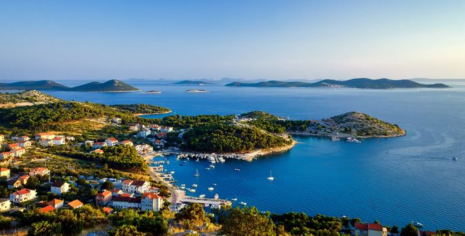 Blick auf die Küste mit mehreren kleinen Inseln, bewaldeten Hügeln, Häusern mit roten Dächern und Segelbooten im blauen Meer