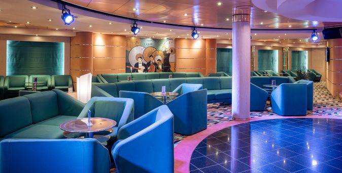 Loungebereich Cotton Club auf der MSC Opera mit türkisfarbenen Sitzgruppen, kleiner Bühne und moderner Clubatmosphäre