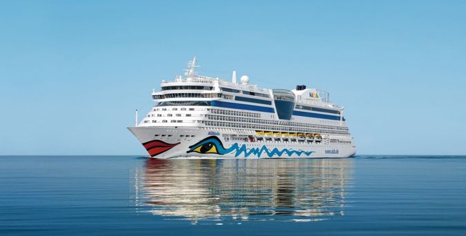 Die AIDAbella spiegelt sich im ruhigen Meerwasser, während das Kreuzfahrtschiff mit seiner auffälligen Bugbemalung fährt