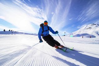 Skifahrer auf einer verschneiten Piste, umgeben von schneebedeckten Bergen und klarem Himmel 