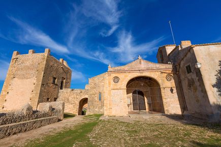 Eingang zum Kloster Puig de Maria auf Mallorca mit historischem Turm und Sandsteinfassade unter blauem Himmel