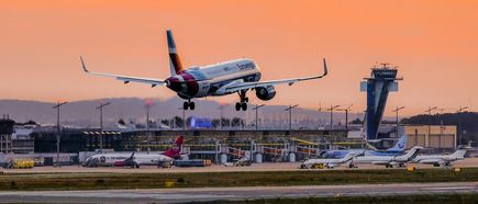 Ein Eurowings-Flugzeug landet bei Sonnenuntergang am Flughafen Nürnberg vor Terminalgebäude, Tower und weiteren Flugzeugen auf dem Vorfeld