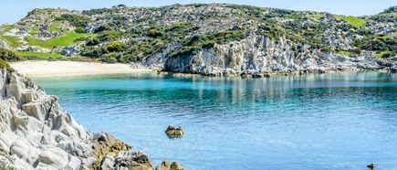 Klares blaues Meer vor felsiger Küste mit grünen Hügeln und Sandstrand in Chalkidiki