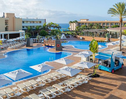Großer Poolbereich des Iberostar Waves Gaviotas Park mit Liegen, Sonnenschirmen, Palmen und einem kleinen Verkaufswagen auf der Terrasse.