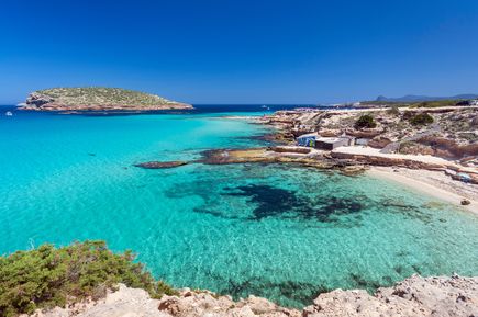 Traumbucht Cala Comte auf Ibiza mit kristallklarem Wasser, Felsen, Sandstrand und der vorgelagerten Insel im Hintergrund