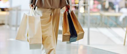 Person in heller Kleidung trägt mehrere Einkaufstüten in einem modernen Einkaufszentrum