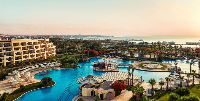 Landschaftsansicht eines Resorts mit mehreren Pools, Liegen und Palmen. Im Hintergrund das Meer.