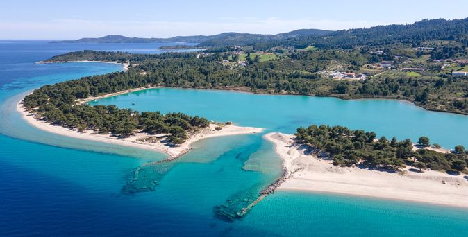 Luftaufnahme einer Küstenlandschaft Glarokavos Beach mit türkisfarbenem Wasser, Sandstränden und bewaldeten Hügeln im Hintergrund.