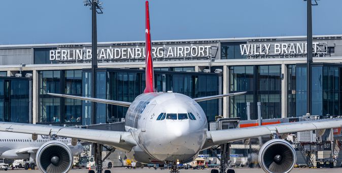 Großes Passagierflugzeug steht vor dem Terminalgebäude des Flughafens Berlin Brandenburg mit der Aufschrift 'BERLIN BRANDENBURG AIRPORT WILLY BRANDT'.