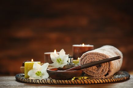 Arrangement aus Wellness-Accessoires wie Handtüchern, Kerzen und Pflegeprodukten auf einem Holztisch