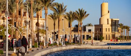 Hafen in Marsa Alam mit Palmen, mehreren Personen am Ufer und einem modernen, runden Turmgebäude