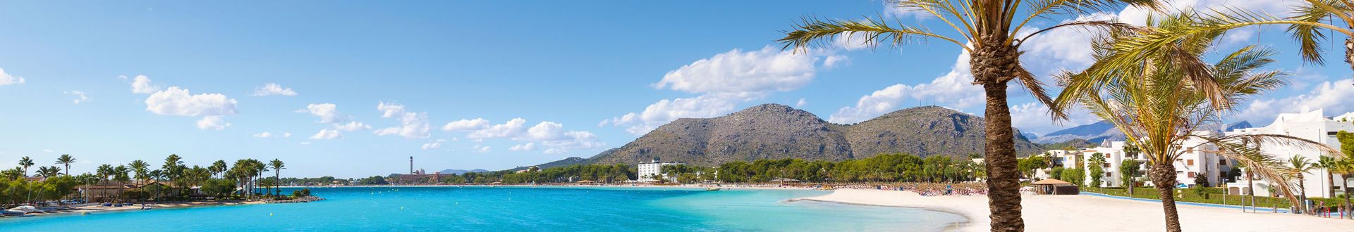 Panoramaaufnahme von Alcúdia auf Mallorca mit weißem Sandstrand, türkisblauem Meer, Palmen und Bergkulisse im Hintergrund