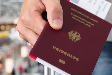 Hand hält deutschen Reisepass mit goldfarbenem Bundesadler und Schriftzug 'REISEPASS' vor unscharfem Bahnhofshintergrund