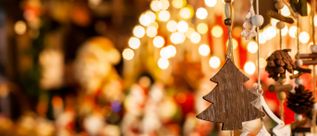 Nahaufnahme eines hölzernen Weihnachtsbaumschmucks vor unscharfem Hintergrund mit warmen Lichtern und weiteren Dekorationen