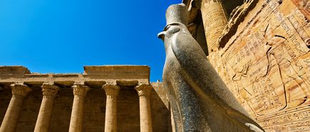 Große steinerne Statue des Gottes Horus mit Falkenkopf vor Säulengang und Wand mit Hieroglyphen im Tempel von Edfu