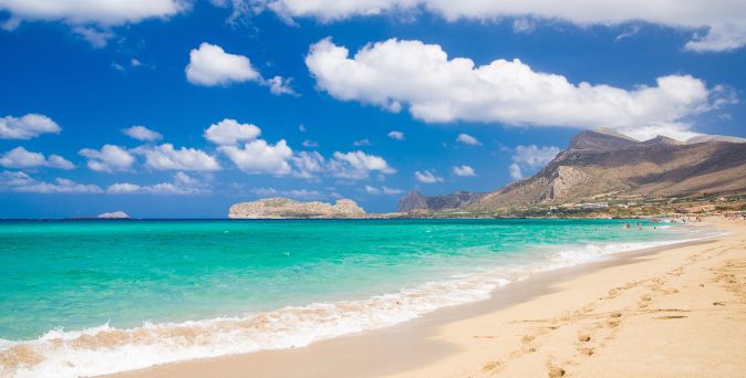 Sandstrand mit türkisfarbenem Meer, bewölktem Himmel und Bergen im Hintergrund an der Küste von Falassarna auf Kreta.
