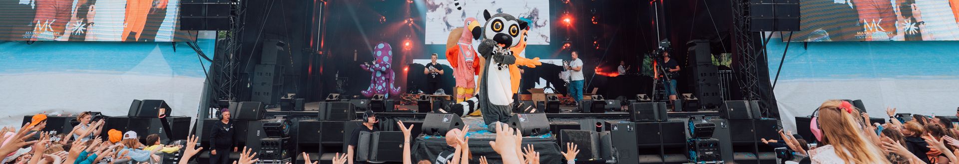 Maskottchen Katta steht auf der großen Bühne des Katta‑Kinderfestivals vor jubelndem Publikum, während Kinder vor der Bühne die Hände ausstrecken