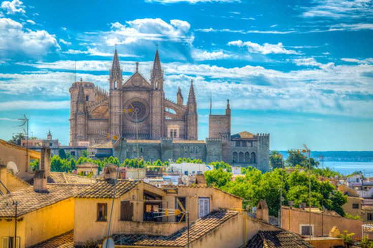Blick auf die Kathedrale von Palma de Mallorca mit den Dächern der Altstadt im Vordergrund und dem Meer im Hintergrund