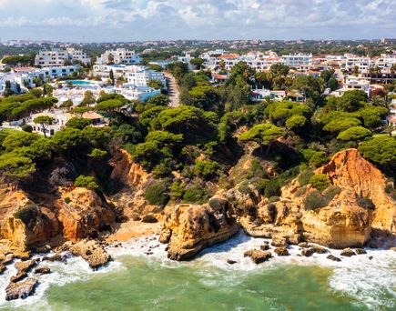 Küstenlinie von Albufeira mit Felsen, Pinien und weißen Gebäuden unter blauem Himmel