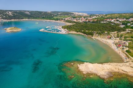 Luftaufnahme der Rajska Plaža auf der Insel Rab in Kroatien mit weitläufigem Sandstrand, türkisblauer Bucht, Yachthafen und dem Küstenort Lopar im Hintergrund.