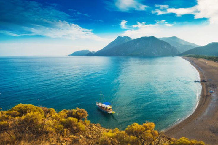 Weitläufiger Strand von Çıralı an der türkischen Riviera mit klarem türkisblauem Meer, bewaldeten Bergen und einem kleinen Boot