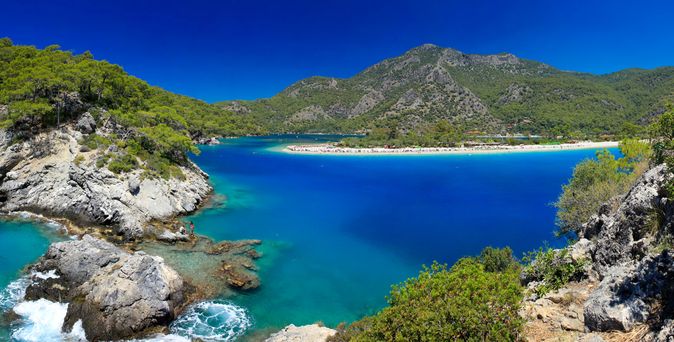 Bucht mit türkisblauem Wasser, umgeben von bewaldeten Bergen und felsigen Ufern unter klarem blauem Himmel
