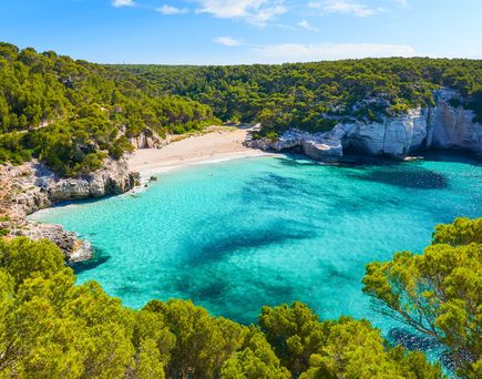 Idyllische Bucht Cala Mitjaneta auf Menorca mit weißem Sandstrand, türkisfarbenem Wasser und von Klippen umgeben