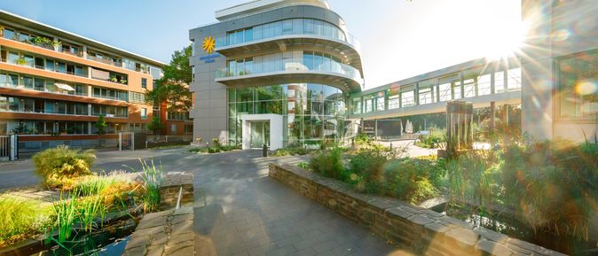 Modernes Firmengebäude von schauinsland-reisen mit Glasfassade, angrenzendem Teich und begrüntem Hof bei Sonnenschein.