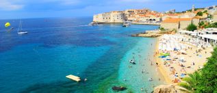 Banje-Strand in Dubrovnik, Kroatien, mit klarem türkisblauem Meer, Badegästen und Blick auf die Altstadt