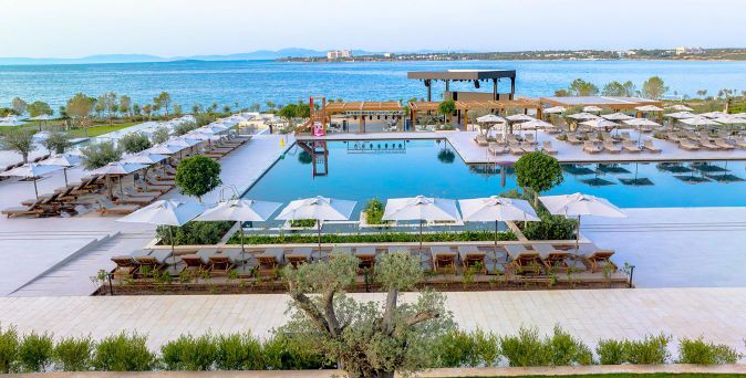 Großer rechteckiger Hotelpool mit Liegen und Sonnenschirmen am Ufer eines ruhigen Meeres